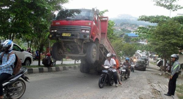 Ilustrasi truk merah dengan roda depan terangkat akibat kelebihan muatan